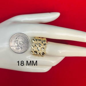 May include: A gold ring with a textured design. The ring is 18 mm wide. The ring is displayed on a hand.