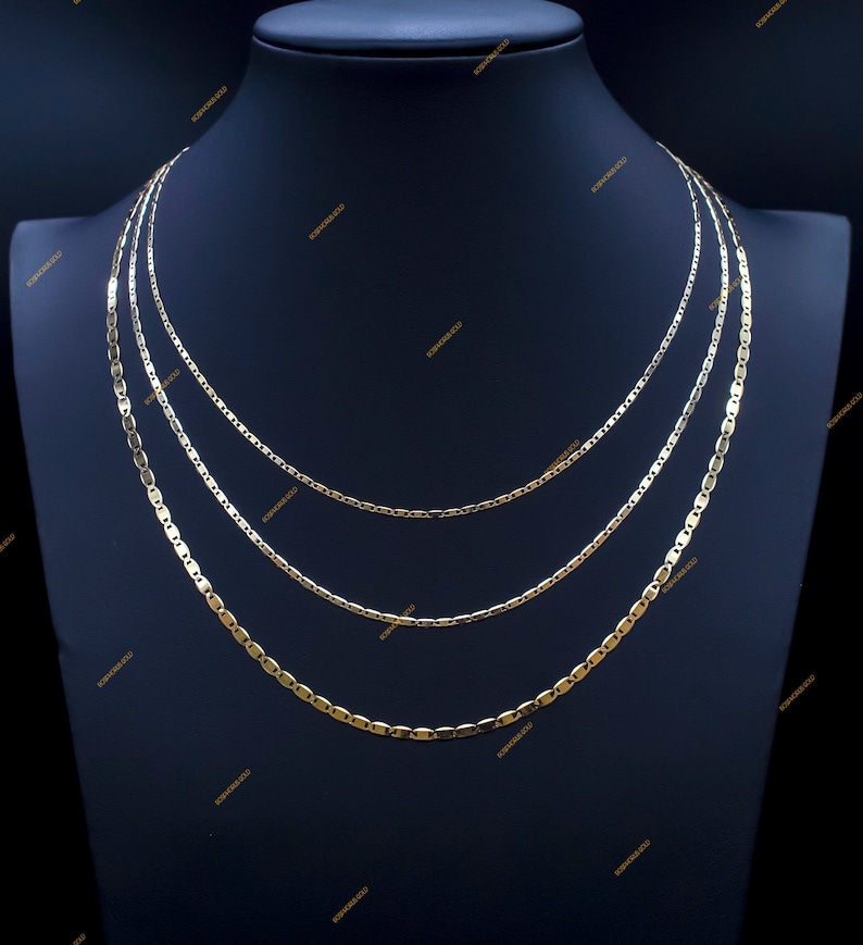 May include: Three gold chains of different lengths and styles, displayed on a black mannequin bust. The chains are all made of a shiny, polished metal.