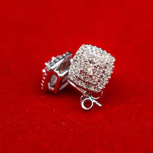 May include: A pair of silver earrings with a square-shaped diamond setting. The earrings are on a red velvet background.