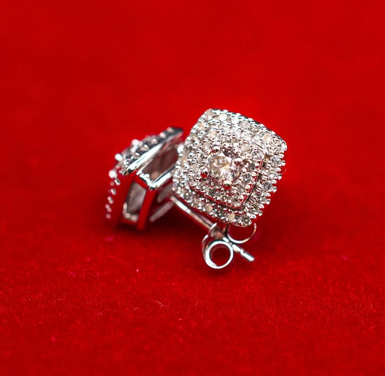 May include: A pair of silver earrings with a square-shaped diamond setting. The earrings are on a red velvet background.