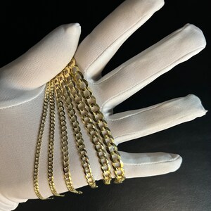 May include: A set of five gold chains of varying widths and lengths. The chains are arranged in a fan shape on a white surface.