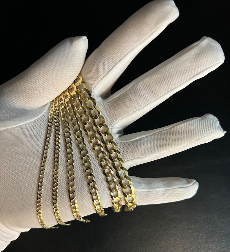 May include: A set of five gold chains of varying widths and lengths. The chains are arranged in a fan shape on a white surface.
