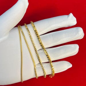 May include: Four gold chains of different widths and lengths, displayed on a white surface.