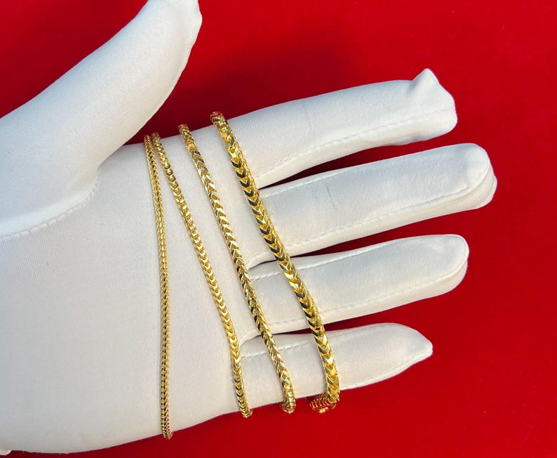 May include: Four gold chains of different widths and lengths, displayed on a white surface.