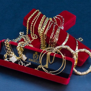 May include: A collection of gold chains, bracelets, and earrings displayed in red velvet boxes. The jewelry is arranged in a decorative manner, showcasing the intricate designs and craftsmanship. The boxes feature the inscription "Josh's Gold" and the initials "BG".