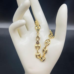 K&ouml;nnte beinhalten: Ein goldfarbenes Ankerkettenarmband mit einem Karabinerverschluss.
