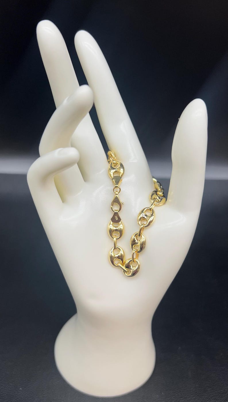 K&ouml;nnte beinhalten: Ein goldfarbenes Ankerkettenarmband mit einem Karabinerverschluss.