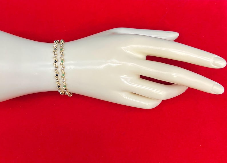 May include: Two gold bracelets with alternating black and green gemstones. The bracelets are on a mannequin's wrist.