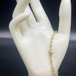 May include: A gold bracelet with alternating emerald green and clear round stones.