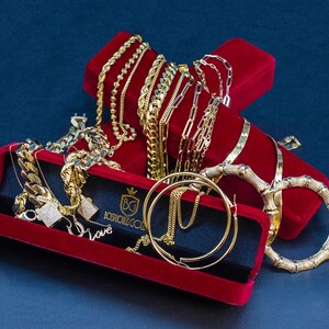 May include: A collection of gold chains, bracelets and earrings in red velvet boxes. The boxes have the words "Boss Moves Gold" printed on them.