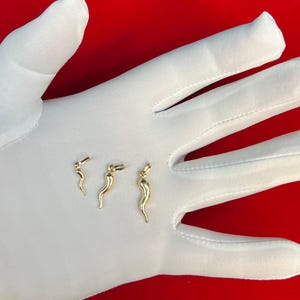 May include: Three gold-coloured pepper charm pendants of varying sizes. The charms are shaped like a pepper and are displayed on a white surface.