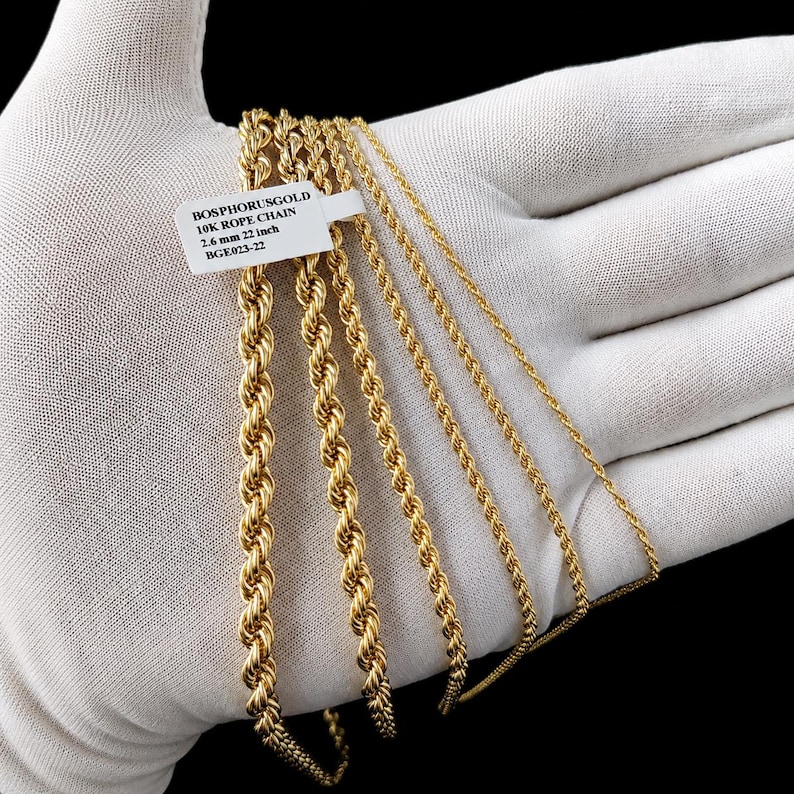 May include: Several gold-colored rope chains of varying thicknesses are displayed. A tag reads "BOSPHORUSGOLD 10K ROPE CHAIN 2.6 mm 22 inch BGE023-22". The chains are presented on a white surface.
