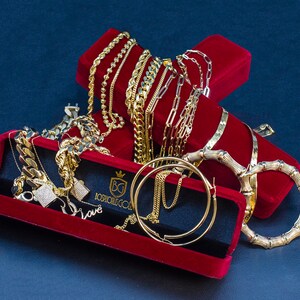 May include: A collection of gold chains, bracelets, and earrings displayed in red velvet boxes. The jewelry is arranged in a decorative manner, showcasing the intricate designs and craftsmanship. The boxes feature the inscription "Josh's Gold" and the initials "BG".