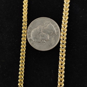 May include: A gold chain necklace with a curb link pattern. The chain is laid out on a black surface next to a US quarter.