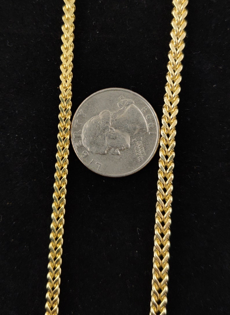 May include: A gold chain necklace with a curb link pattern. The chain is laid out on a black surface next to a US quarter.