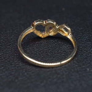 May include: A gold ring with two intertwined hearts, one of which is set with small sparkling stones.