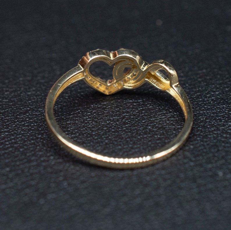 May include: A gold ring with two intertwined hearts, one of which is set with small sparkling stones.