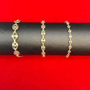 Könnte beinhalten: Drei goldene Kettenarmbänder in verschiedenen Längen, auf einer schwarzen Oberfläche präsentiert.