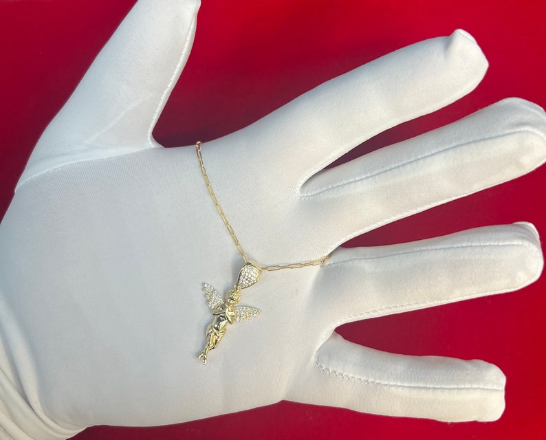 Puede incluir: Un collar de cadena de oro con un peque&ntilde;o colgante de &aacute;ngel incrustado con cristales transparentes.