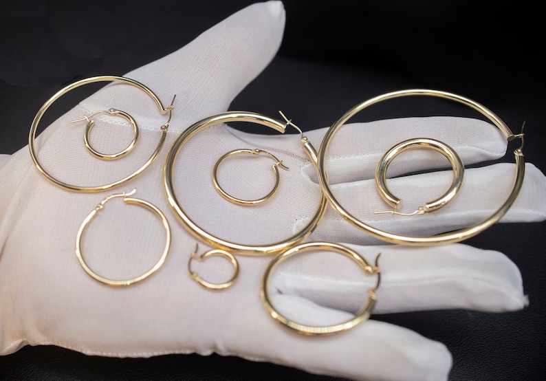 May include: A set of six gold hoop earrings of varying sizes. The earrings are displayed on a white surface.