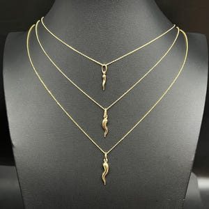 May include: Three gold necklaces with a small gold horn pendant on each. The necklaces are layered on a black mannequin bust.