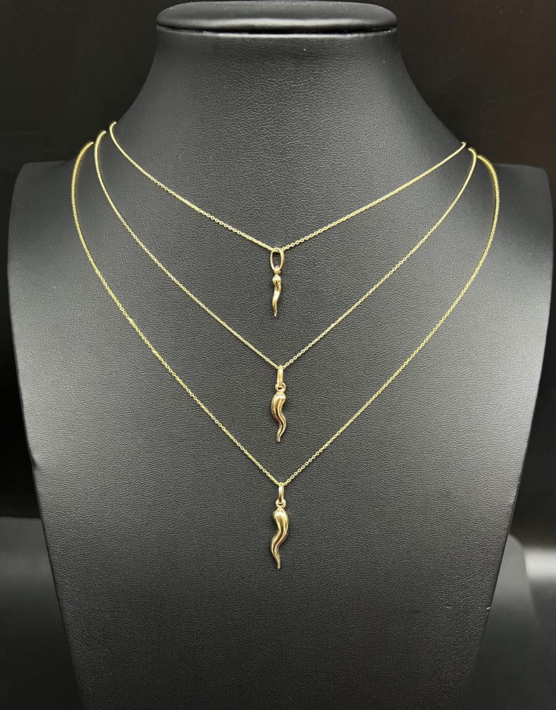 May include: Three gold necklaces with a small gold horn pendant on each. The necklaces are layered on a black mannequin bust.