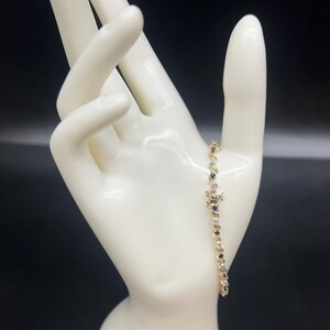 May include: A gold bracelet with alternating blue and white gemstones. The bracelet is on a white mannequin hand.