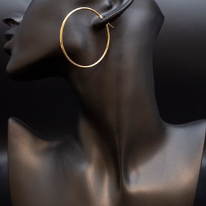 May include: Gold hoop earrings on a black mannequin head.