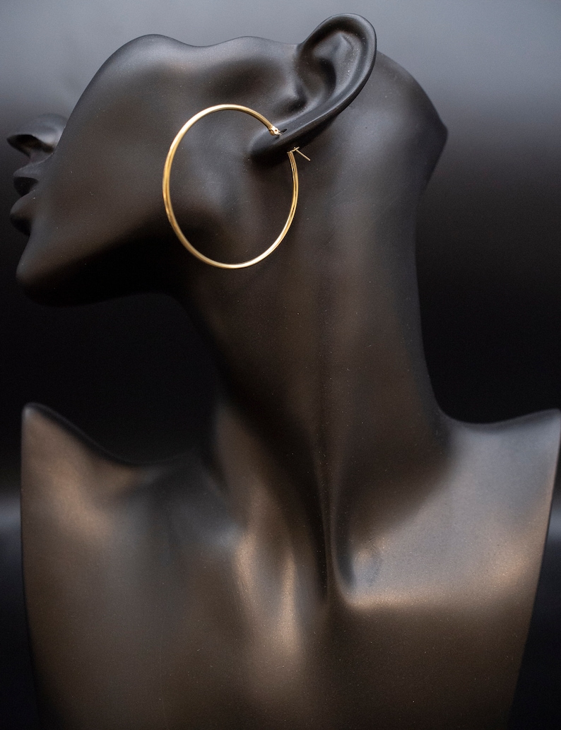 May include: Gold hoop earrings on a black mannequin head.