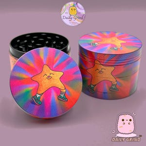 A four piece Metal Tobacco Grinder with a colourful striking design. The grinder features a star very happy in the middle of the image with a multi coloured explosion behind him. The inside of the grinder is black. The background of the image is dark green and The Daily Grind logo is visible in the corner of the image