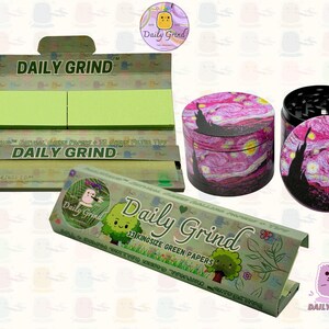 A dark Purple packet and a Green box with the text 'Daily Grind' on both and ‘Kingsize Purple Papers' on one and ‘Kingsize Green Papers’ on the other. Both boxes open showing green papers in one and purple in the other. There is a tobacco grinder with a classic pink piece of art underneath it and The 'Daily Grind' logo is in the corner of the image