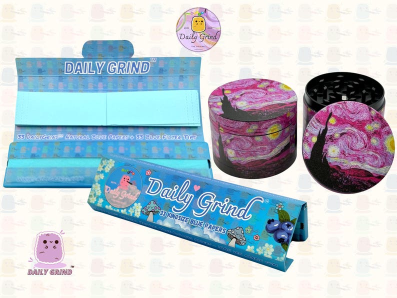 A deep blue and light blue box with the text 'Daily Grind' and ‘Kingsize Blue Papers' on it. The box is open and there are blue papers inside. There is a tobacco grinder with a cute pink art design on it next to the box and The 'Daily Grind' logo is in the corner of the image