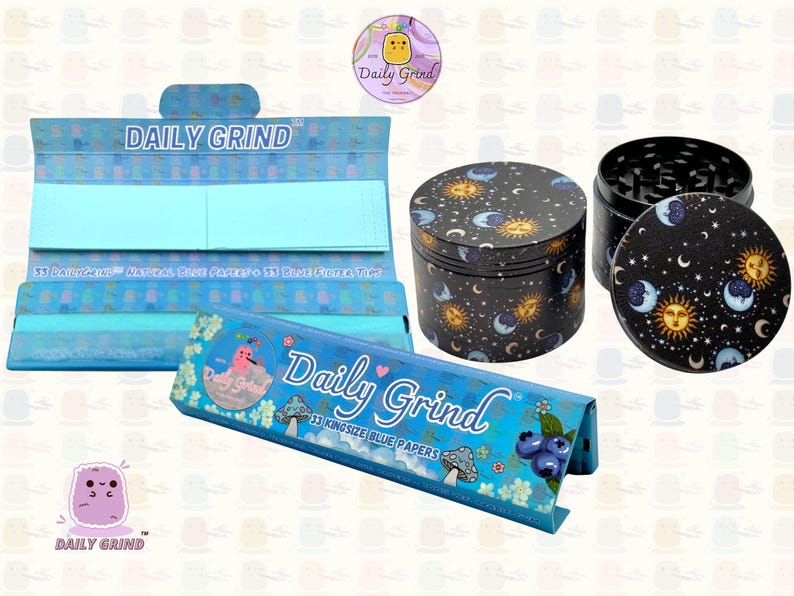 A deep blue and light blue box with the text 'Daily Grind' and ‘Kingsize Blue Papers' on it. The box is open and there are blue papers inside. There is a tobacco grinder with a cartoon sun and moon astrology design on it next to the box and The 'Daily Grind' logo is in the corner of the image