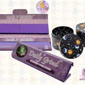 A dark Purple packet and a Green box with the text 'Daily Grind' on both and ‘Kingsize Purple Papers' on one and ‘Kingsize Green Papers’ on the other. Both boxes open showing green papers in one and purple in the other. There is a tobacco grinder with a cartoon sun and moon astrology design on it underneath it and The 'Daily Grind' logo is in the corner of the image
