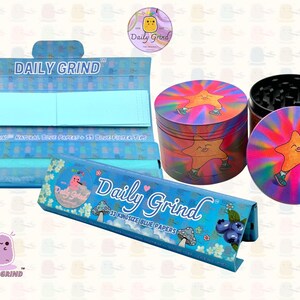 A deep blue and light blue box with the text 'Daily Grind' and ‘Kingsize Blue Papers' on it. The box is open and there are blue papers inside. There is a tobacco grinder with a very happy and confident star character in the middle with rays of light behind him next to the box and The 'Daily Grind' logo is in the corner of the image