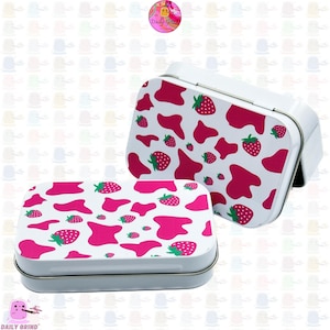 May include: Two white metal tins with a pink and white cow print design featuring strawberries. The tins are open and the lids are off.