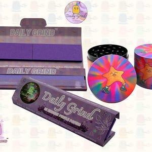 A dark Purple packet and a Green box with the text 'Daily Grind' on both and ‘Kingsize Purple Papers' on one and ‘Kingsize Green Papers’ on the other. Both boxes open showing green papers in one and purple in the other. There is a tobacco grinder with a very happy and confident star character in the middle with rays of light behind him underneath it and The 'Daily Grind' logo is in the corner of the image