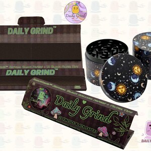 A black and green box with the text 'Daily Grind' and Kingsize Black Papers' on it. The box is open and there are black papers inside. There is a tobacco grinder with a cartoon sun and moon astrology design on it next to the box and the 'Daily Grind' logo is in the corner of the image