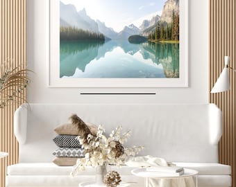 Puede incluir: Una fotografía enmarcada de un lago de montaña con un reflejo de las montañas en el agua. El lago está rodeado de árboles y montañas. La foto está en un marco blanco y está colgada en una pared blanca.