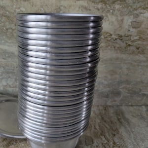 May include: A stack of small, brushed metal bowls. The bowls are silver-colored and have a rounded shape with a slightly flared rim. The bowls are stacked neatly, with the rims aligned. The background is a textured, neutral surface.