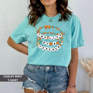 chalky mint Comfort Colors® shirt with colorful beaded bracelet design spelling "The Life Of A Teacher", surrounded by school-themed icons
