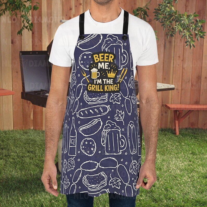 May include: Navy blue apron featuring a white food and beer design. The apron has the text "BEER ME, I'M THE GRILL KING!" in yellow and white. Black straps and buttons complete the design. Ideal for barbecues.
