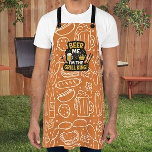 May include: An orange apron with a white food and beer pattern. The apron has the text "BEER ME, I'M THE GRILL KING!" in black and yellow. The apron has black straps and is worn by a person.