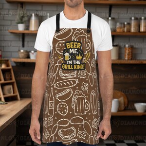 May include: Brown apron with a white food-themed pattern, including hot dogs, burgers, and beer mugs. The apron features the text "BEER ME, I'M THE GRILL KING!" in a black and yellow design. Black straps and a white shirt complete the look.