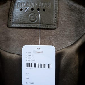May include: Close-up of a green suede jacket with a leather tag that reads "BLANKNYC". A white tag is attached with the size "L" and the color "GRN/VERT".