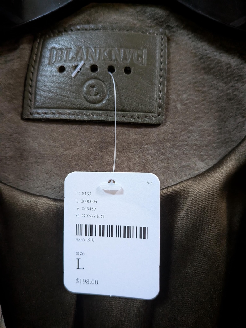 May include: Close-up of a green suede jacket with a leather tag that reads "BLANKNYC". A white tag is attached with the size "L" and the color "GRN/VERT".