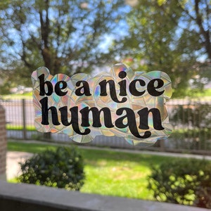 May include: A holographic sticker with the text "be a nice human" in black lettering.