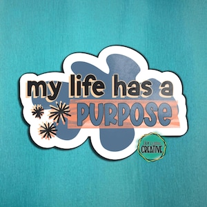 May include: A sticker with the phrase "my life has a PURPOSE" in a stylized font. The sticker has a white border and features a blue and orange color scheme with decorative starbursts. The sticker also includes the text "Hero Creative".
