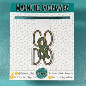 May include: Green and gold magnetic bookmark with the words "GO & DO" in a stylized font. The bookmark is on a white background with a small pattern of gray dots.