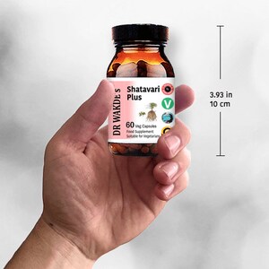 Op de afbeelding: Een bruine glazen fles met een wit etiket waarop "DR WAKDE'S Shatavari Plus 60 Veg Capsules Food Supplement Suitable for Vegetarians" staat. De fles is 10 cm hoog en heeft een groene en bruine illustratie van een plant op het etiket.